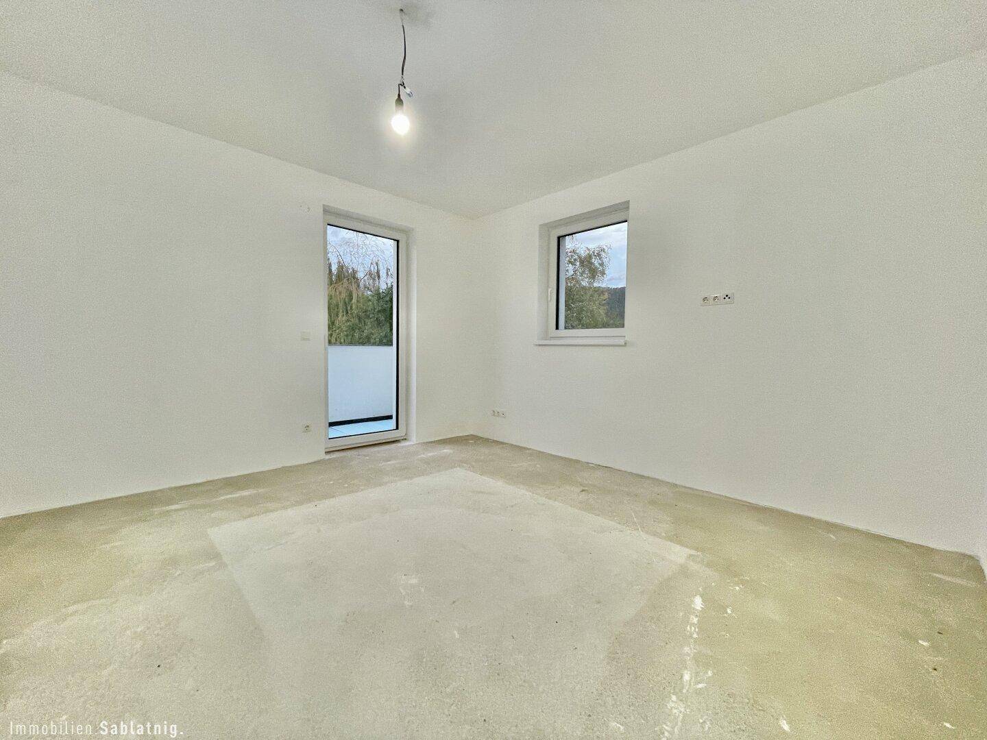Leeres Schlafzimmer mit Fenster und Zugang nach draußen, noch im Rohbauzustand.