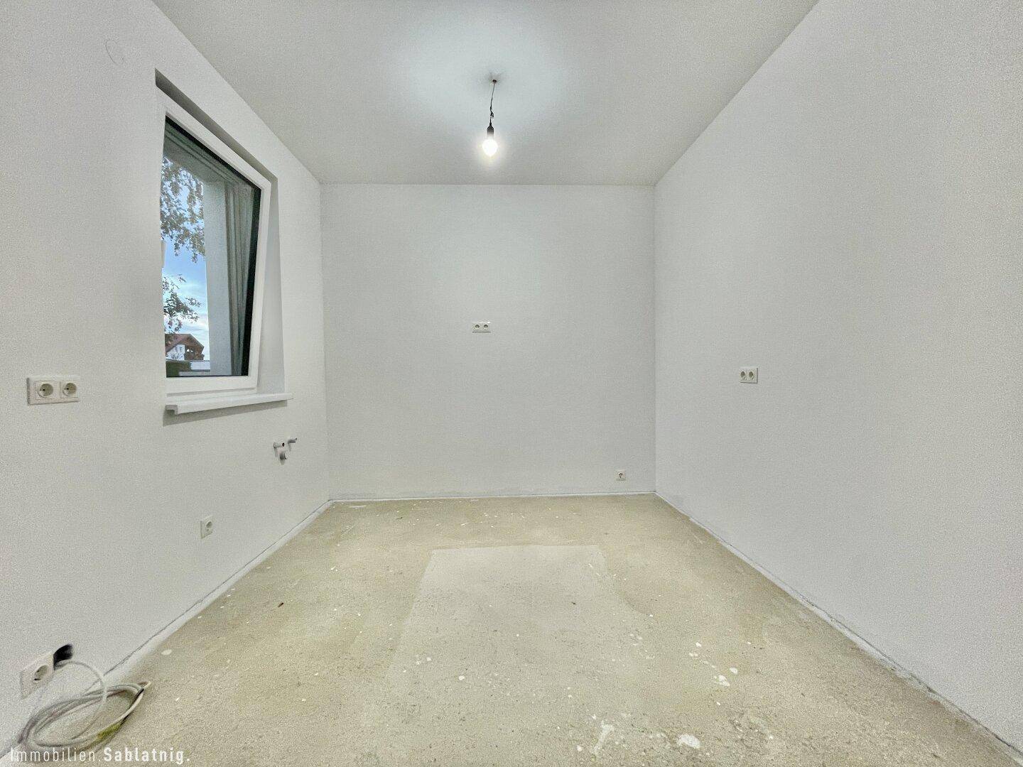 Leerer Raum mit Fenster und Rohboden, ideal als Schlafzimmer oder Büro nutzbar.