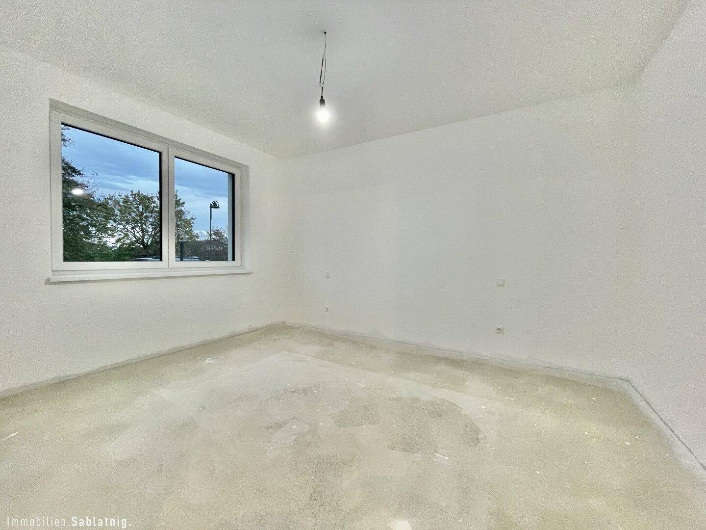 Unmöbliertes Schlafzimmer mit großem Fenster und Rohboden, bereit für den Innenausbau.