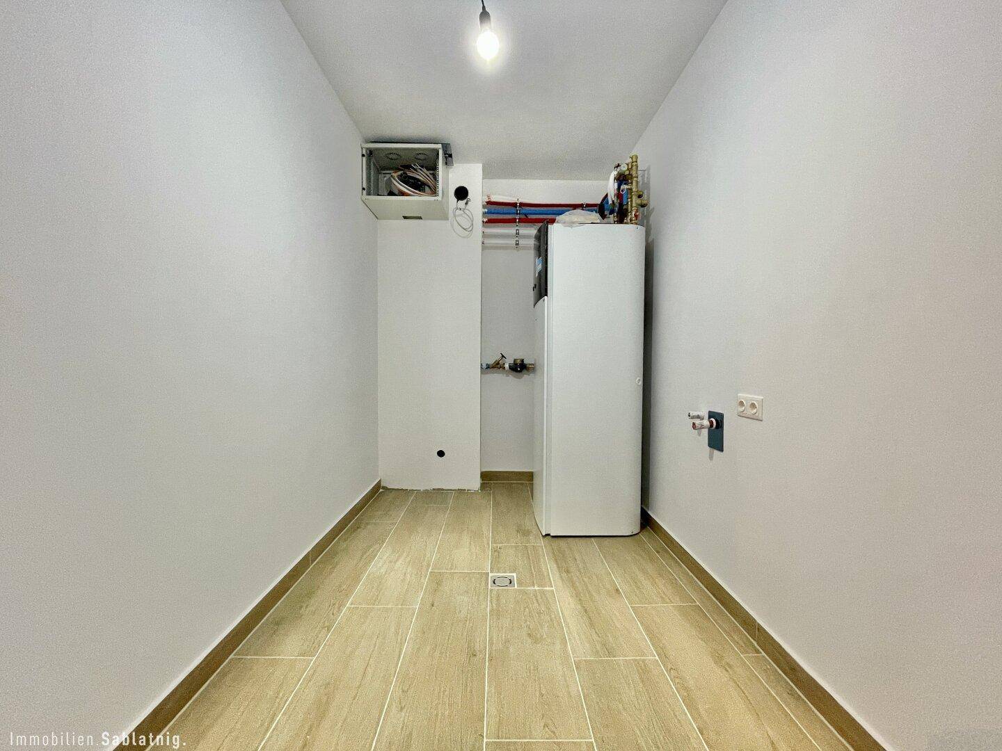 Hauswirtschaftsraum mit Wärmepumpe und gefliestem Boden, bereit für den Betrieb.