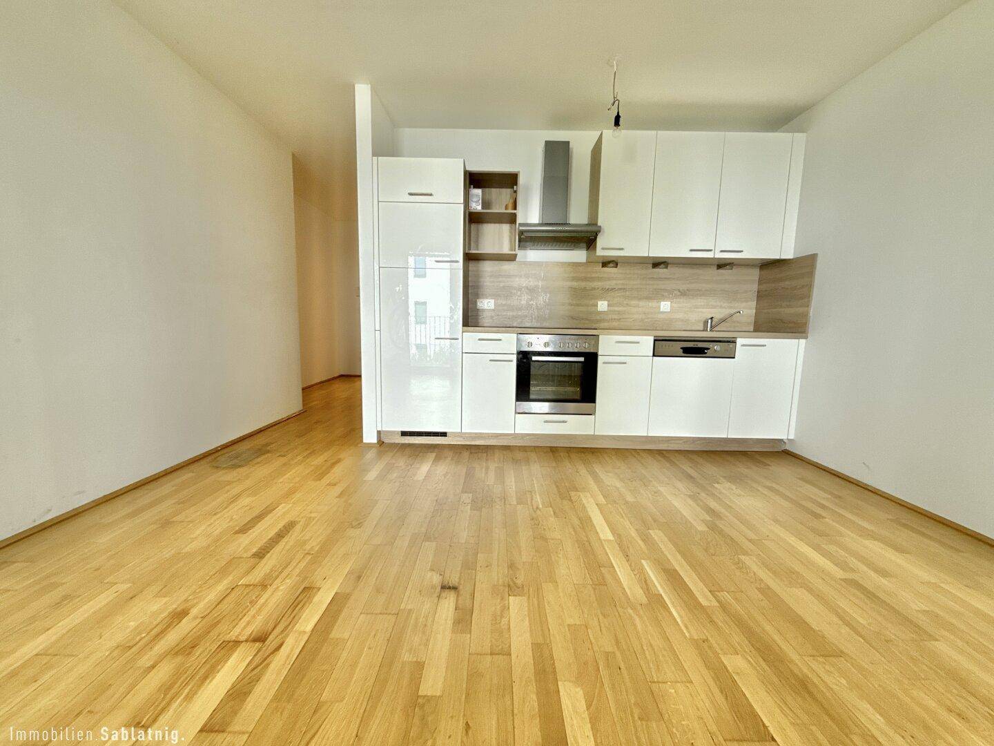 Offene Küche mit weißen Hochglanzfronten, integrierten Geräten und Parkettboden.