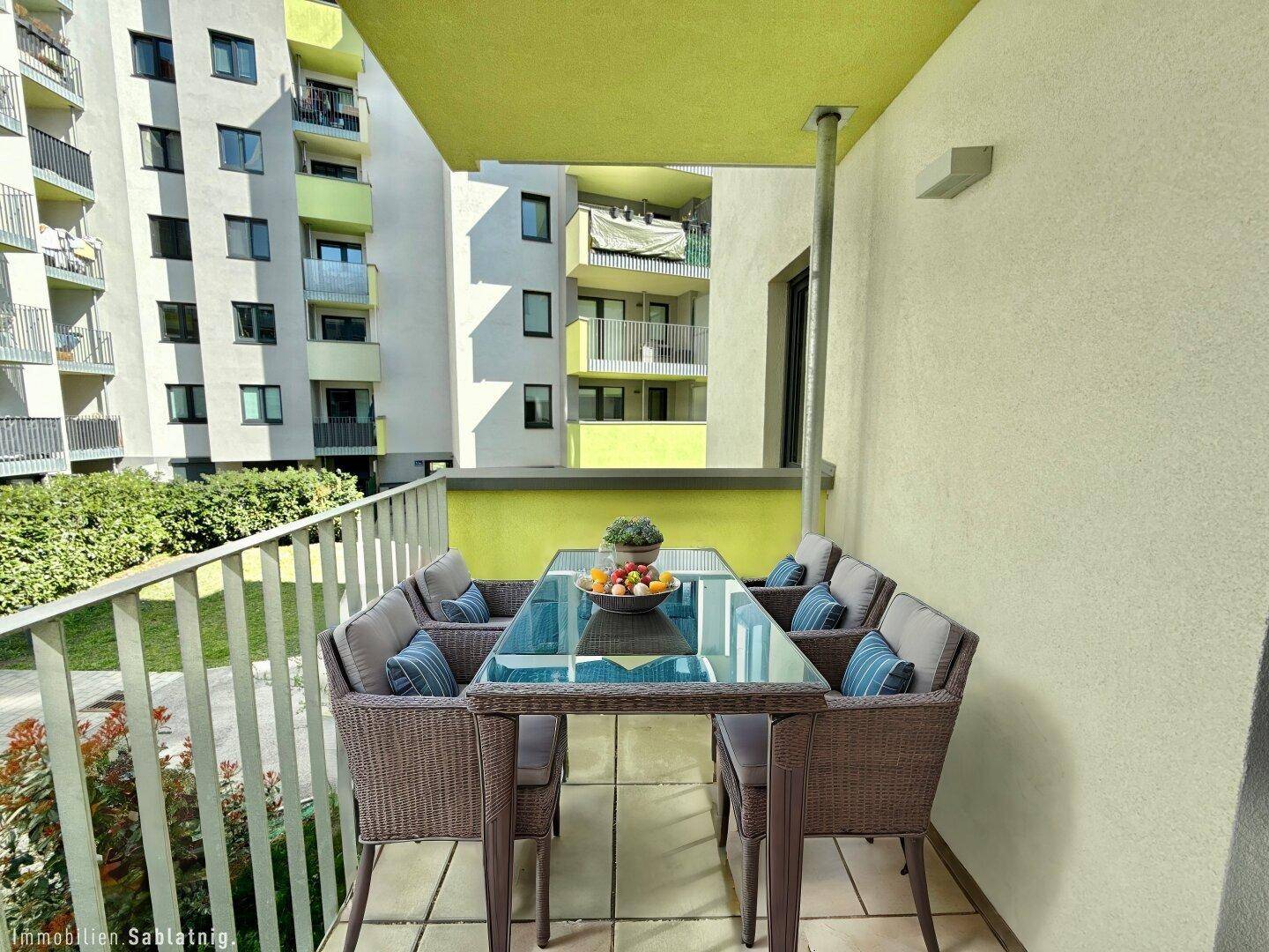 Möblierter Balkon mit Esstisch und Stühlen, umgeben von modernen Wohngebäuden.