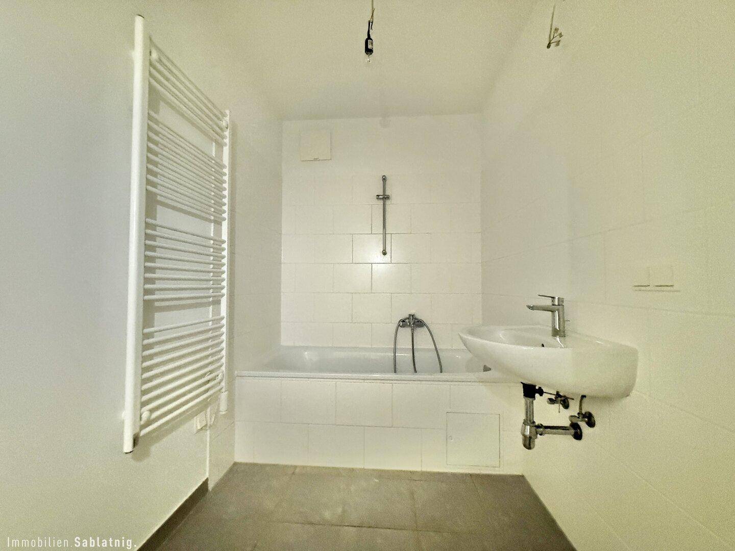 Modernes Badezimmer mit Badewanne, Waschbecken und beheiztem Handtuchhalter.