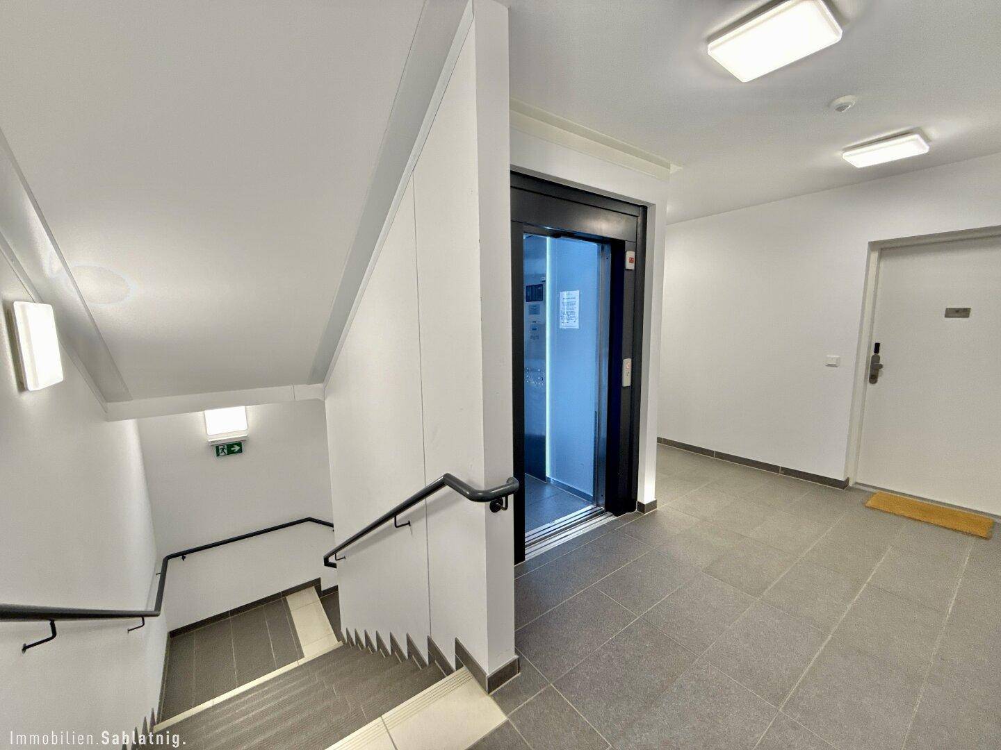Heller Treppenaufgang und Flur mit modernem Aufzug in einem Mehrfamilienhaus.