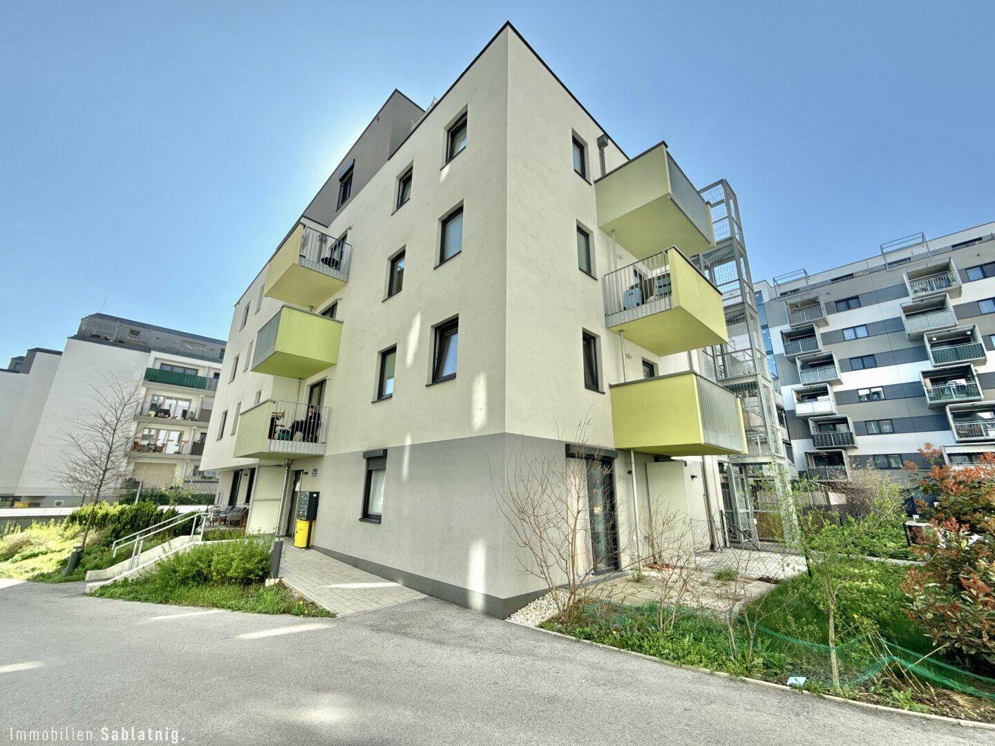 Moderne Wohnanlage mit farbigen Balkonen und gepflegten Grünflächen unter blauem Himmel.