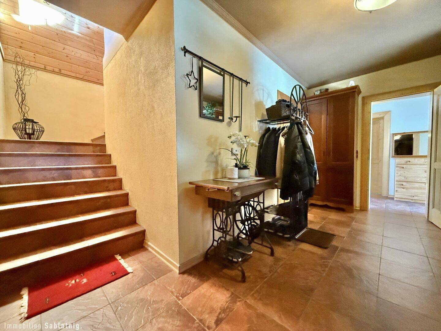 Heller Eingangsbereich mit Treppe, Fliesenboden und Garderobe, die zu den oberen Etagen führt.