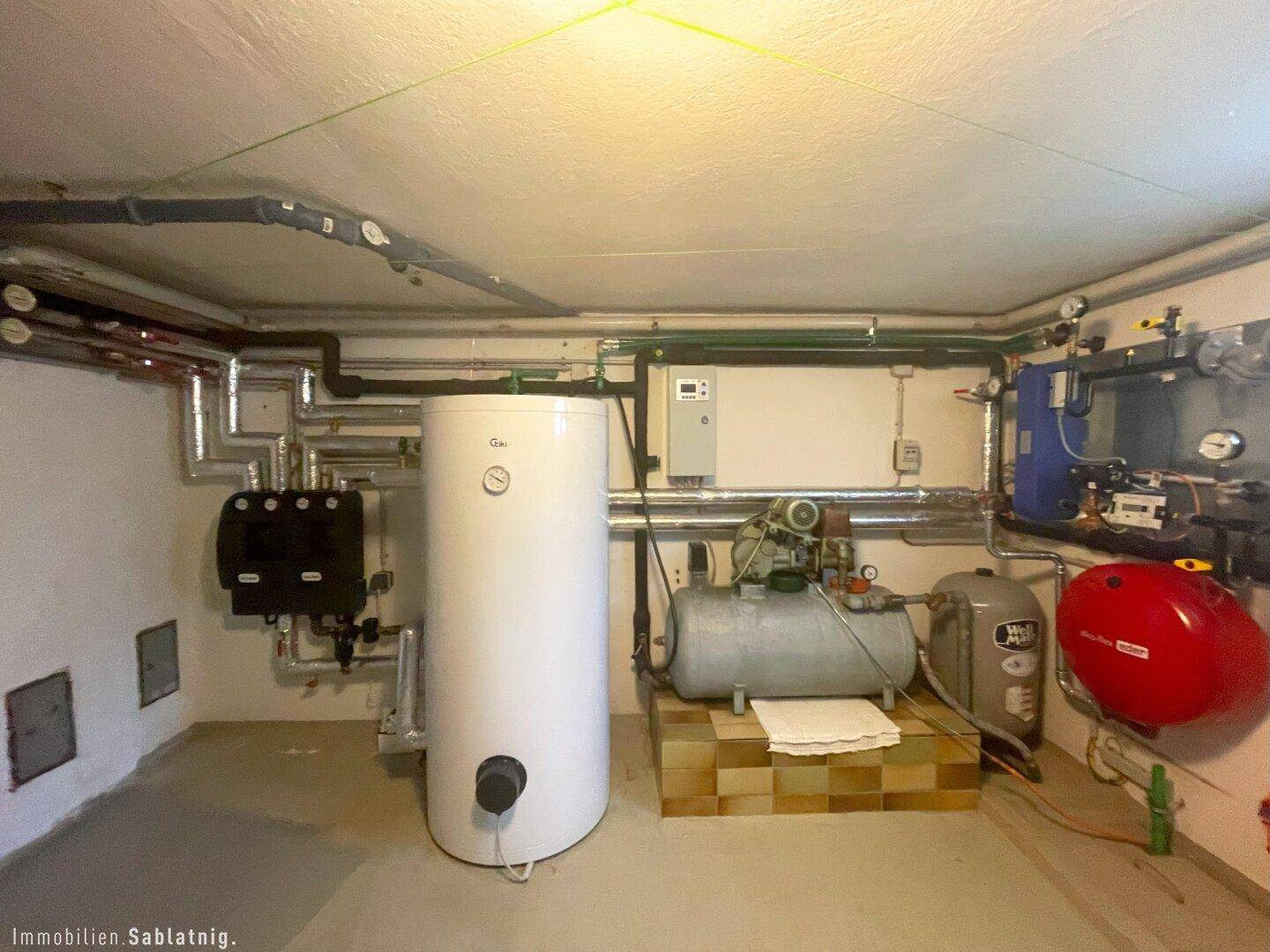 Technikraum im Keller mit Heizungsanlage, Warmwasserspeicher und verschiedenen Rohren.