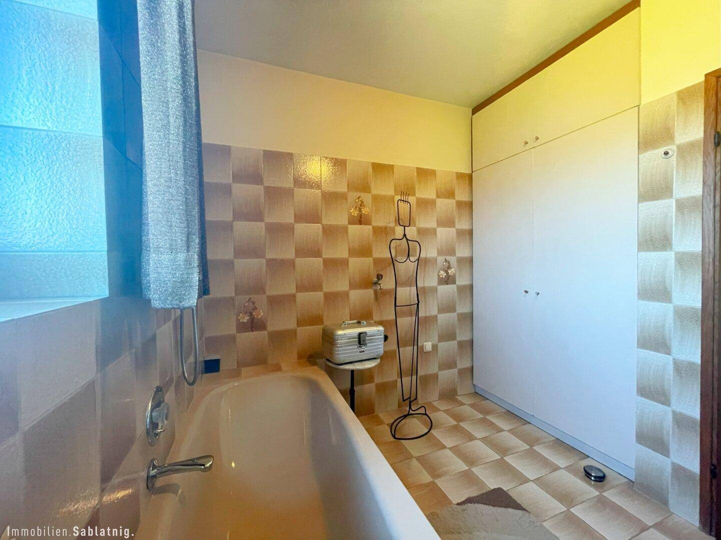 Badezimmer mit Badewanne, karierten Fliesen und Einbauschränken.