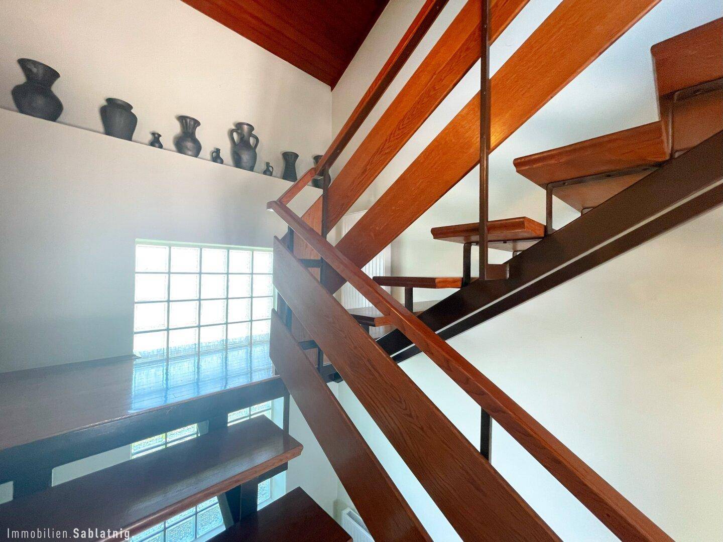 Holztreppe mit Geländer und Glasbausteinfenster, das natürliches Licht hereinlässt.