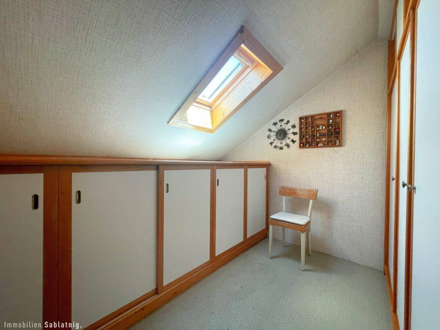 Dachbodenraum mit Dachfenster, Einbauschränken und Teppichboden.