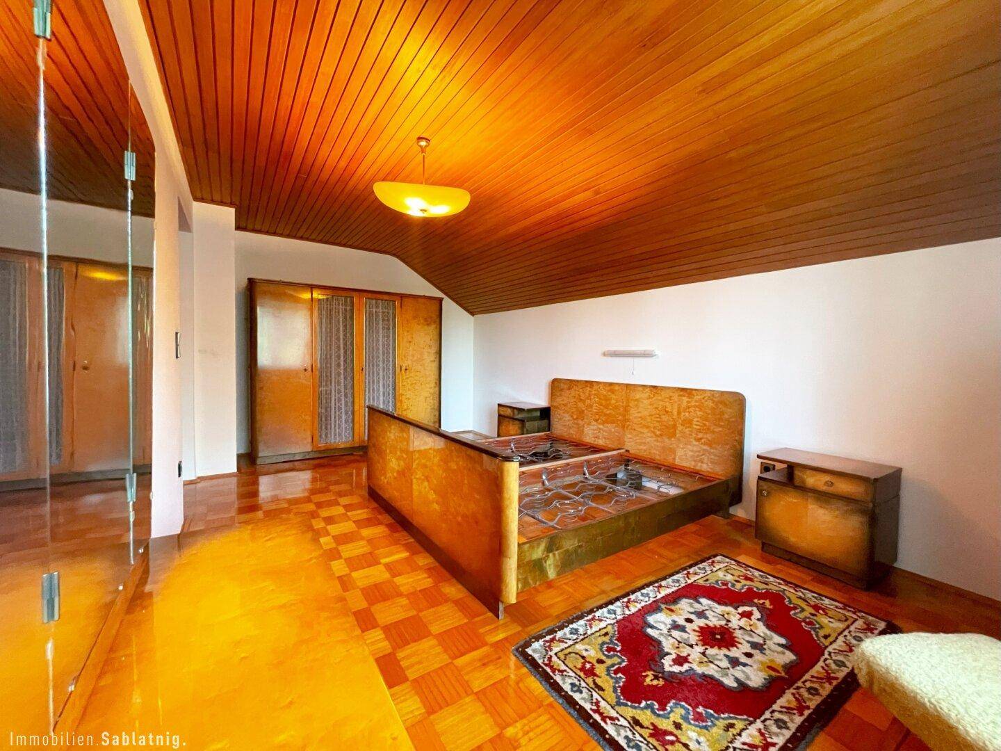 Geräumiges Schlafzimmer mit Holzbett, Holzdecke und Parkettboden.