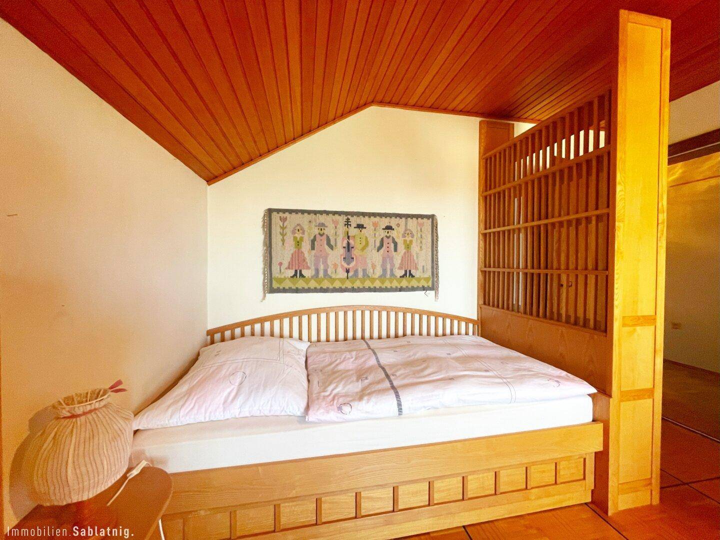 Helles Schlafzimmer mit Holzbett, Holzdecke und traditionellem Wandteppich.