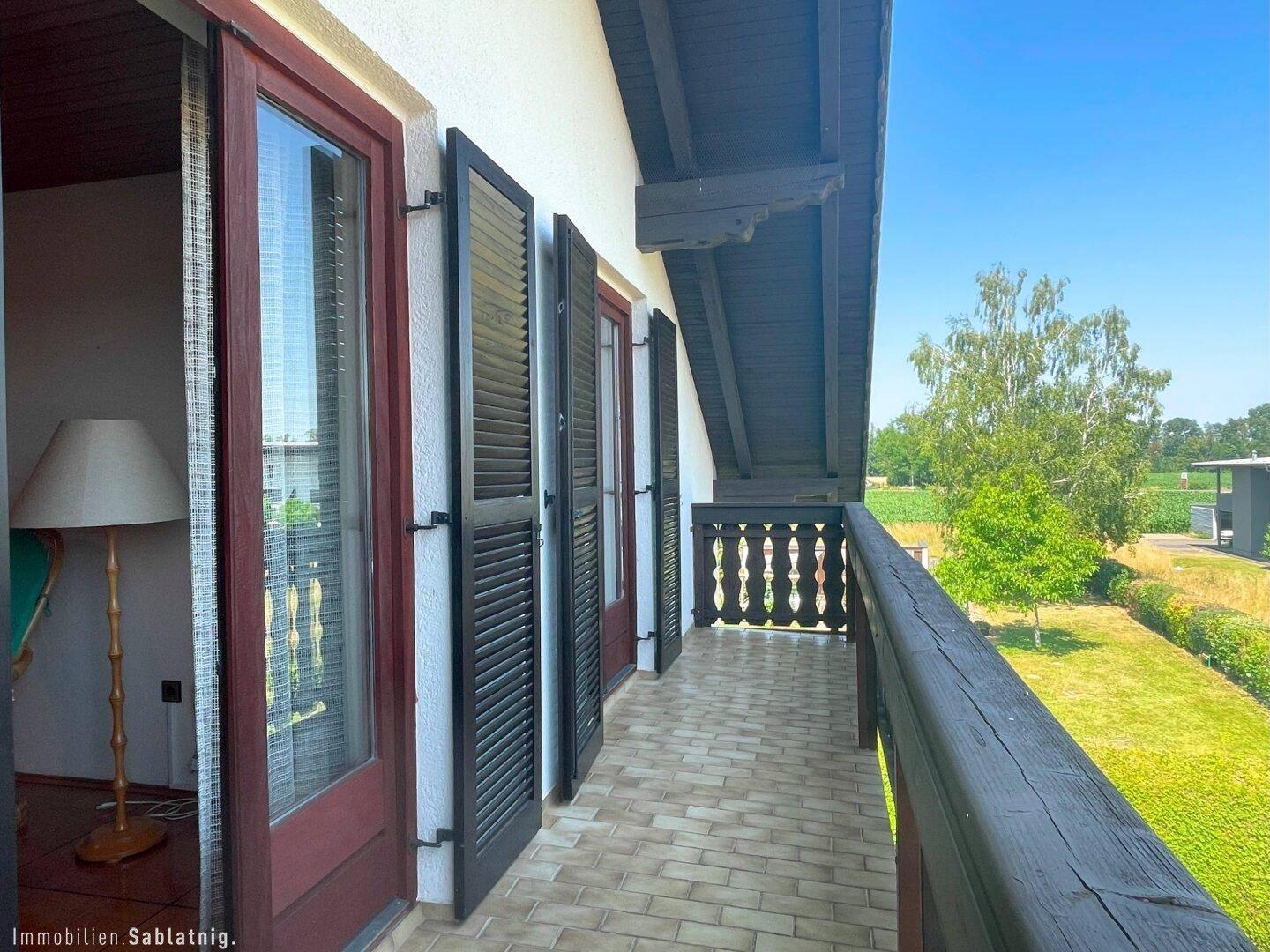 Langer Balkon mit Fliesenboden, Holzgeländer und Blick auf die grüne Landschaft.