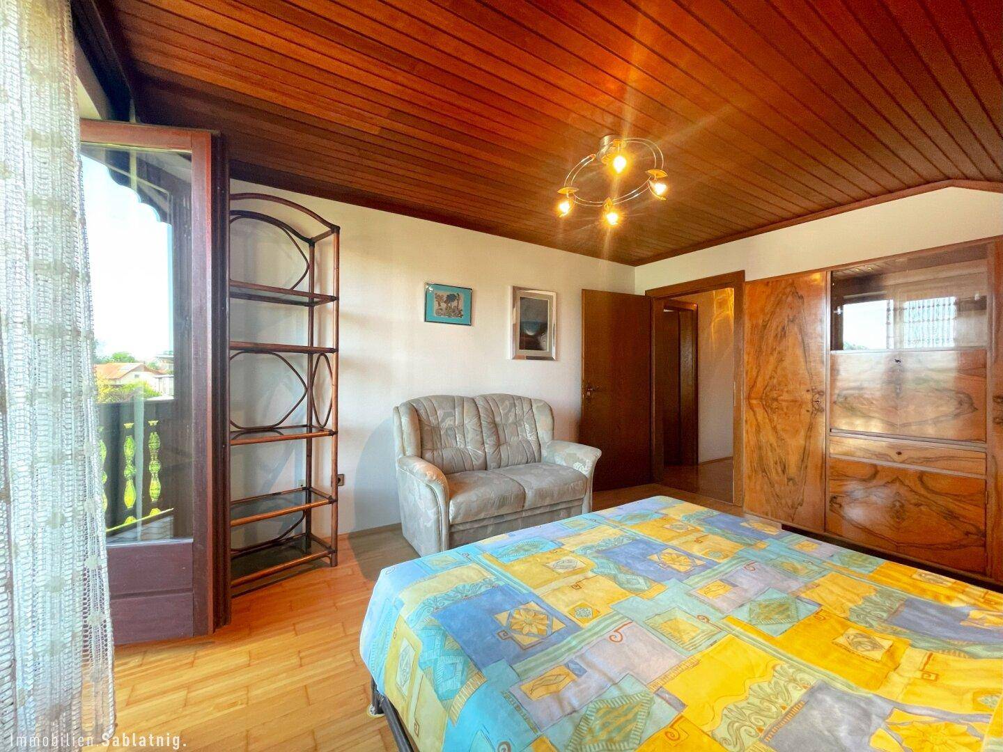 Schlafzimmer mit Doppelbett, Holzdecke und Zugang zu einem Balkon.