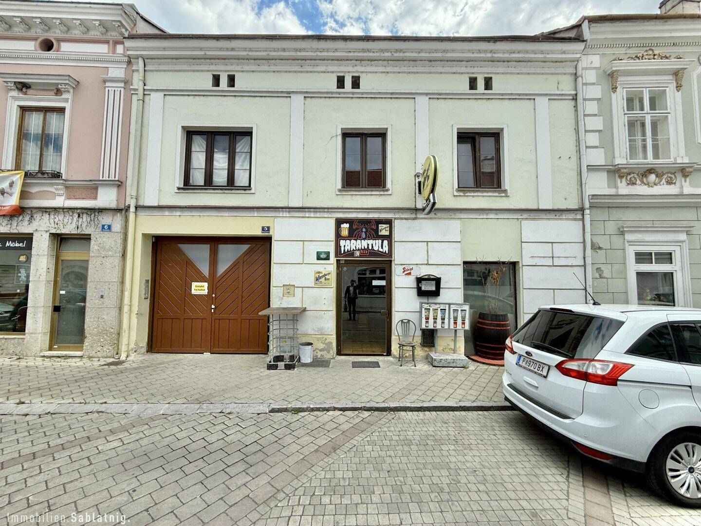 Fassade eines Gebäudes an einer Straße mit Geschäften im Erdgeschoss und geparktem Auto.