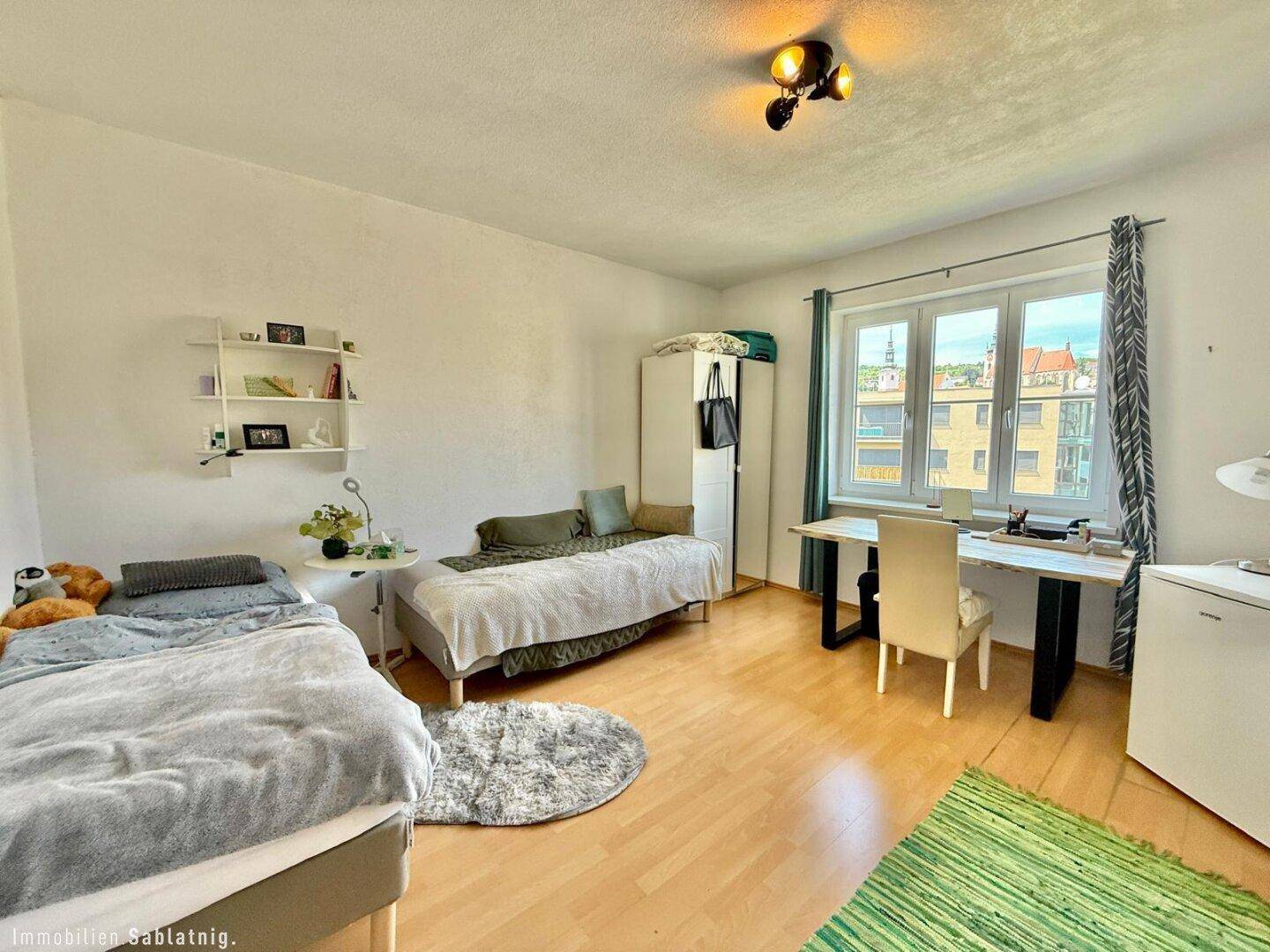 Helles Schlafzimmer mit zwei Einzelbetten, Schreibtisch am Fenster und Holzfußboden.