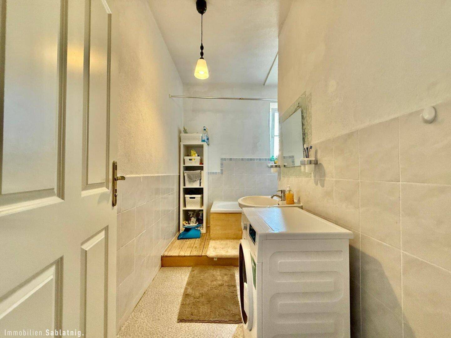 Badezimmer mit Badewanne, Waschbecken, Spiegel und Waschmaschine.