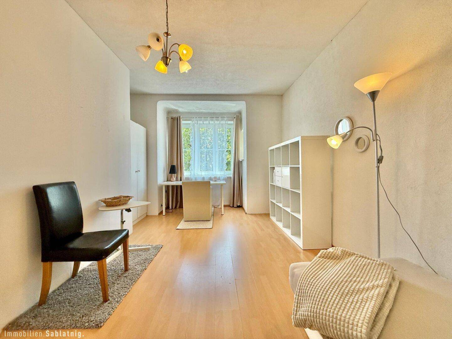 Heller Raum mit Erkerfenster, Schreibtisch, Regal und Holzfußboden.