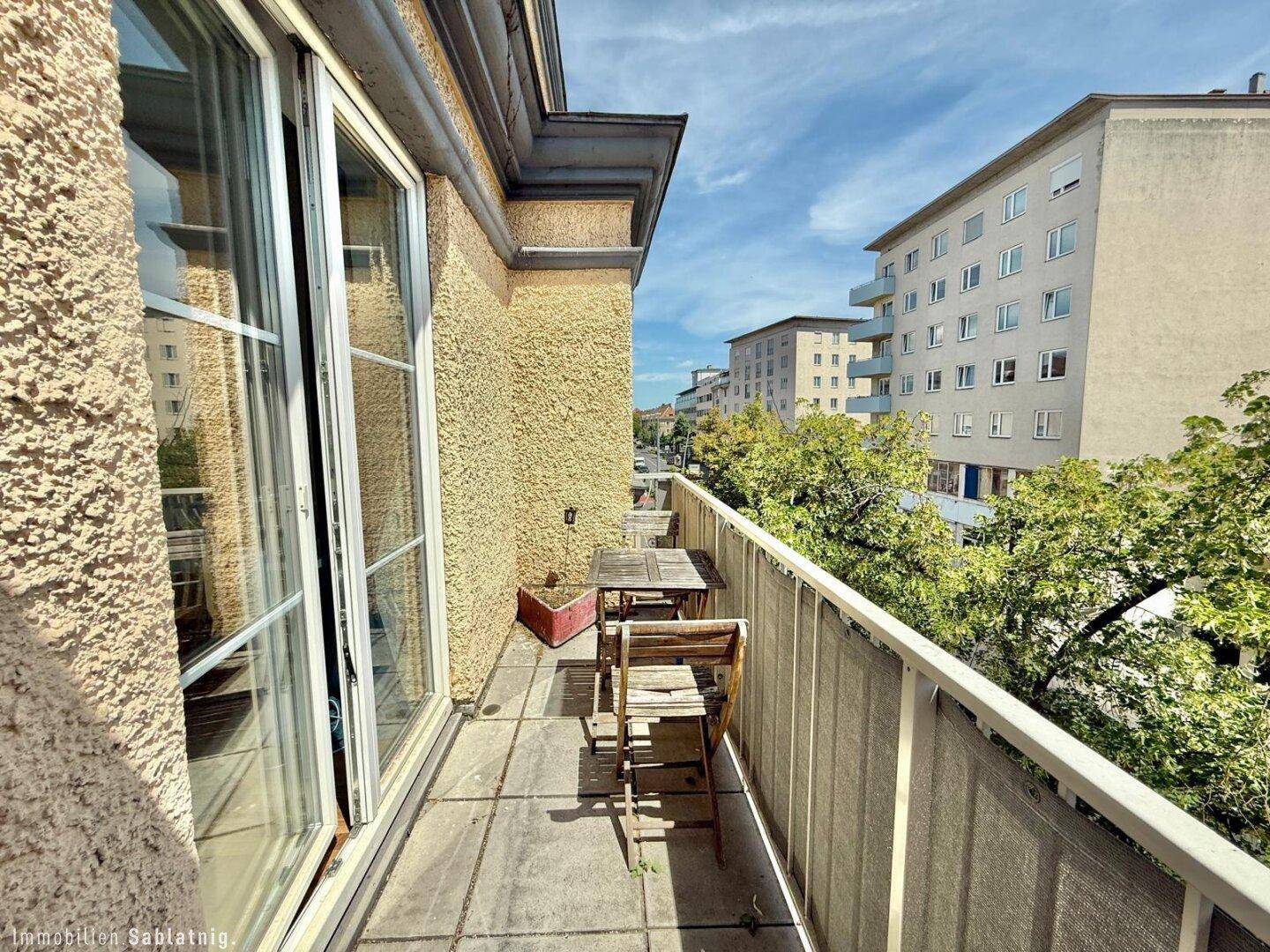 Balkon mit Sitzgelegenheiten und Ausblick auf die umliegenden Gebäude und die Straße.