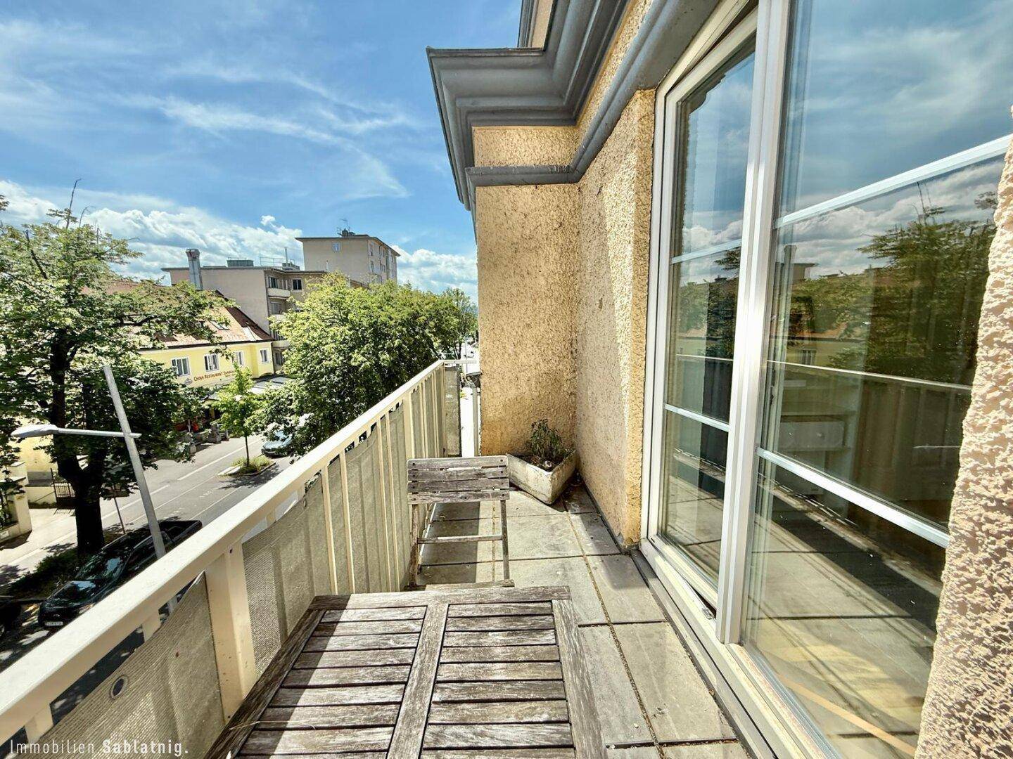 Balkon mit Holzboden, kleinem Tisch und Stühlen mit Blick auf die Straße.
