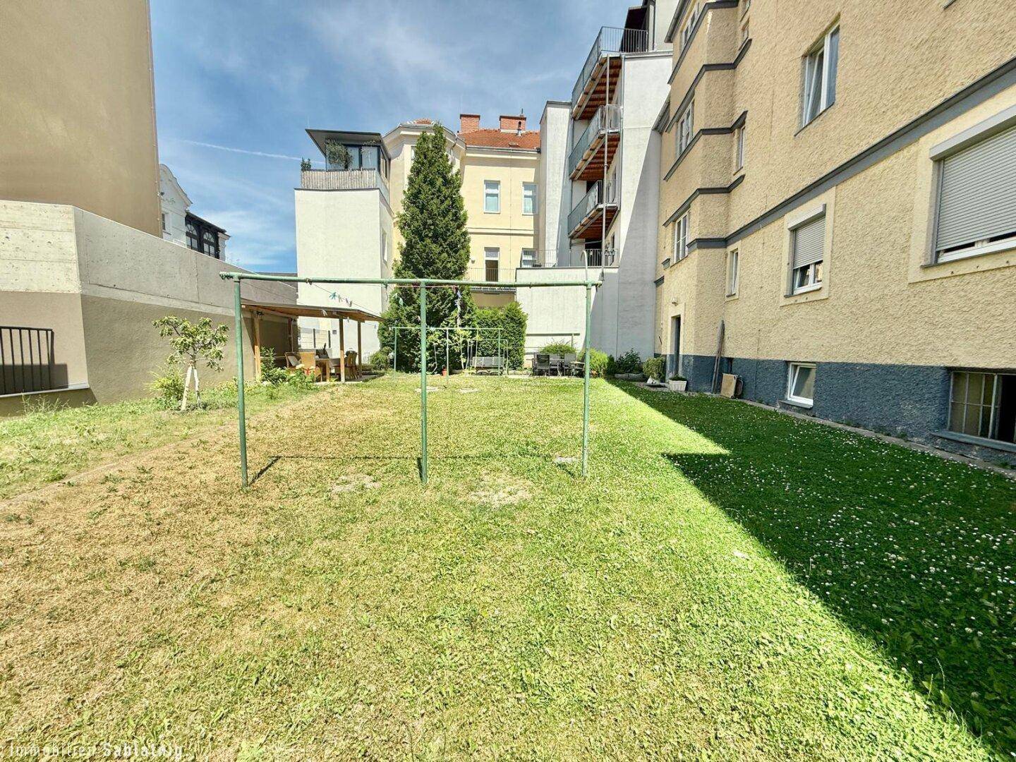 Gemeinschaftlicher Gartenbereich hinter dem Gebäude mit Rasenfläche und Bäumen.