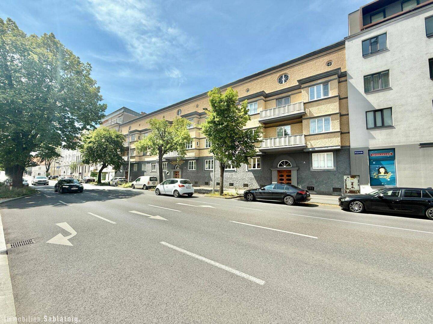 Weitläufige Ansicht der Wohnhausfassade von der Straße mit parkenden Autos.