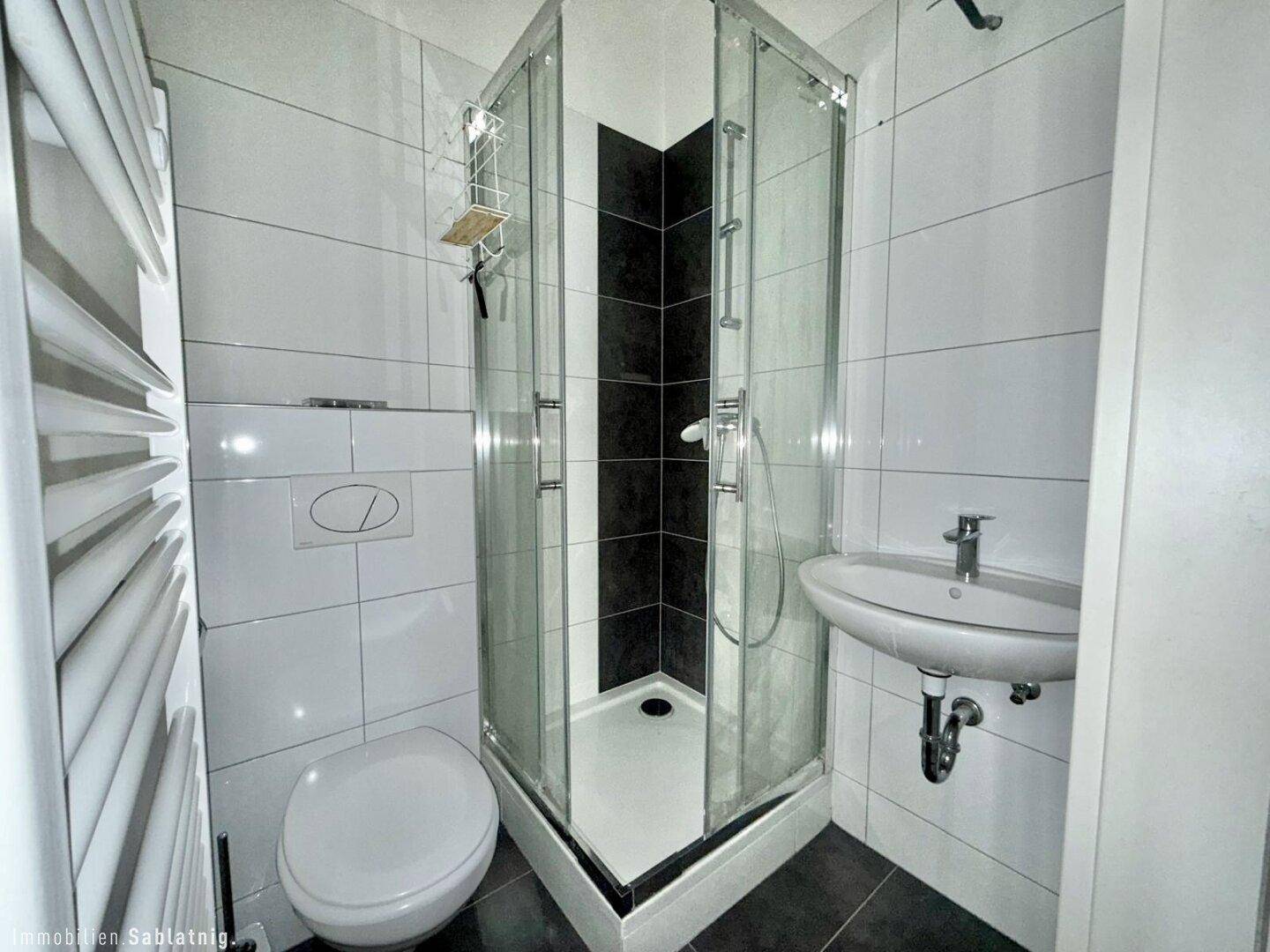 Modernes Badezimmer mit Duschkabine, WC, Waschbecken und beheiztem Handtuchhalter.