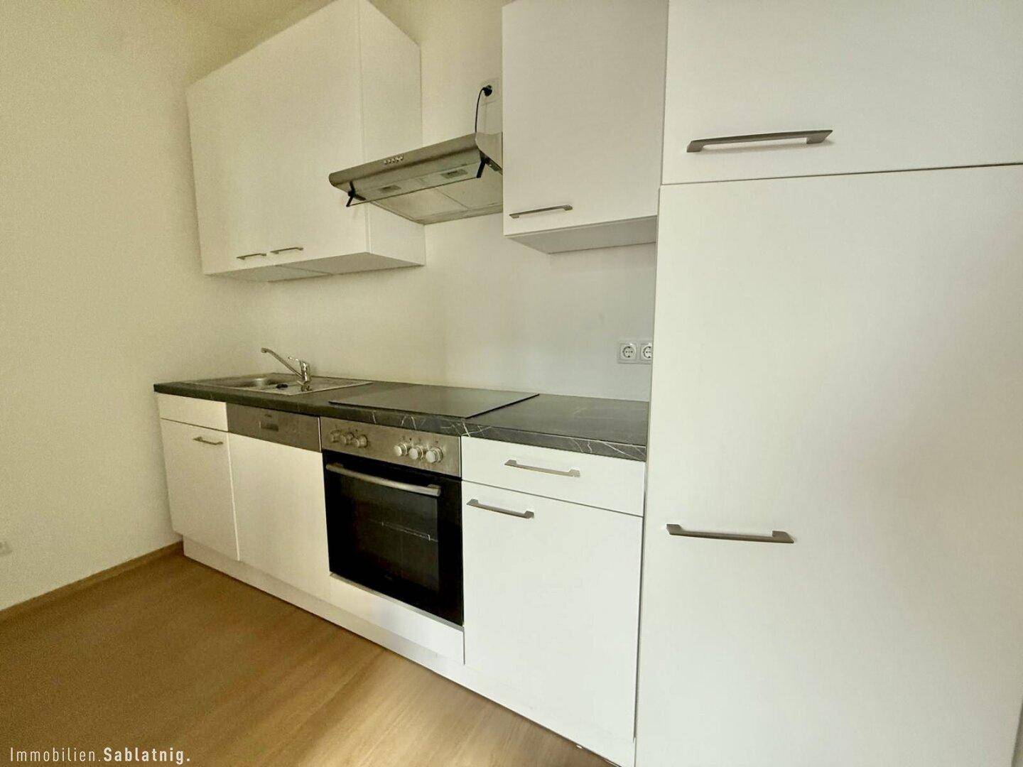 Funktionale Einbauküche mit weißen Schränken, Spüle und integriertem Backofen.