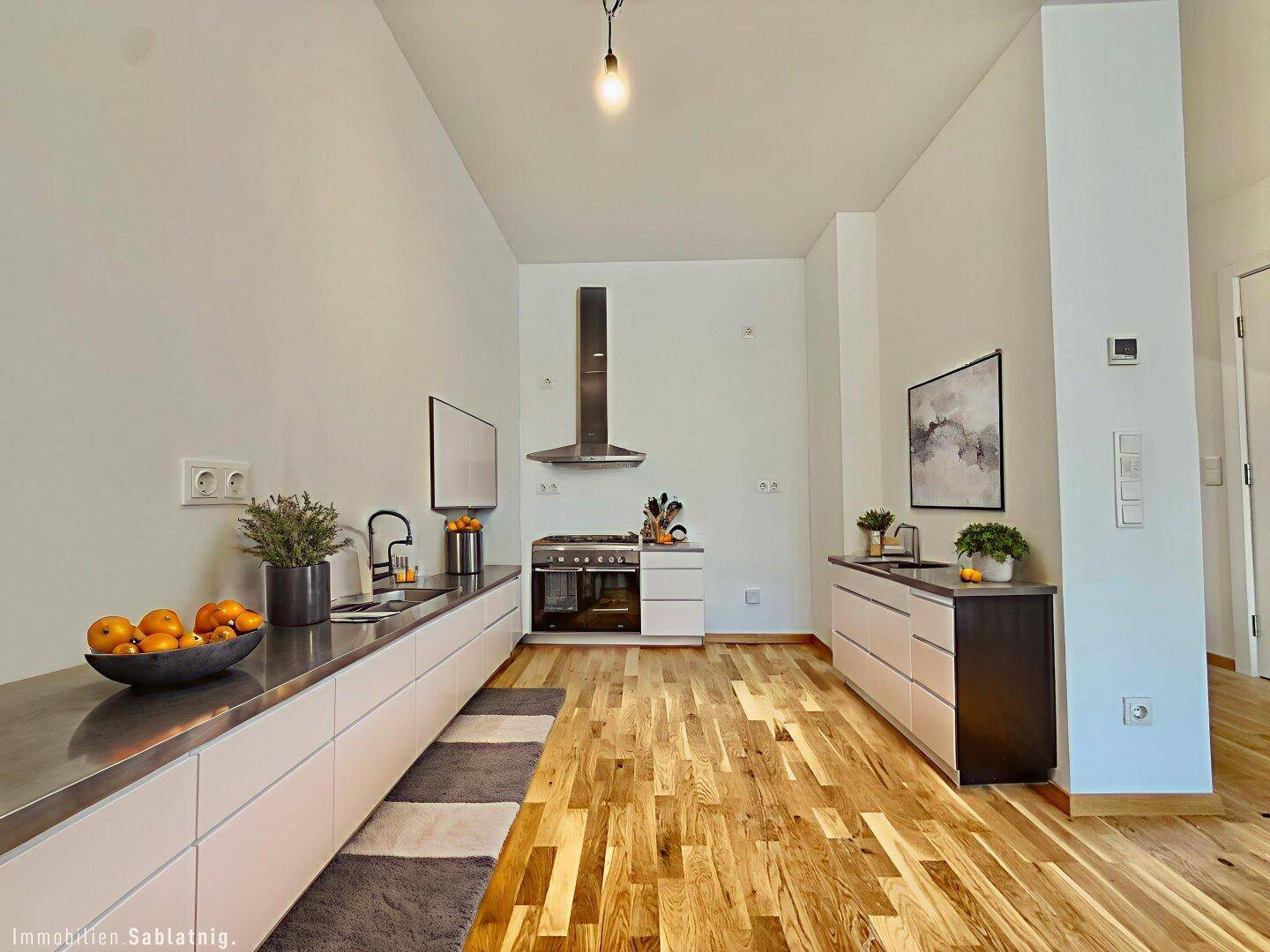 Moderne Küche mit Edelstahlarbeitsplatten, Dunstabzugshaube und Holzboden.
