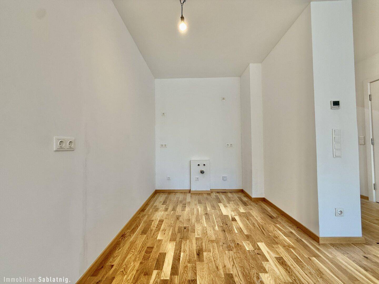Leerer Raum mit Anschlüssen für eine Küche oder Waschküche und Holzboden.