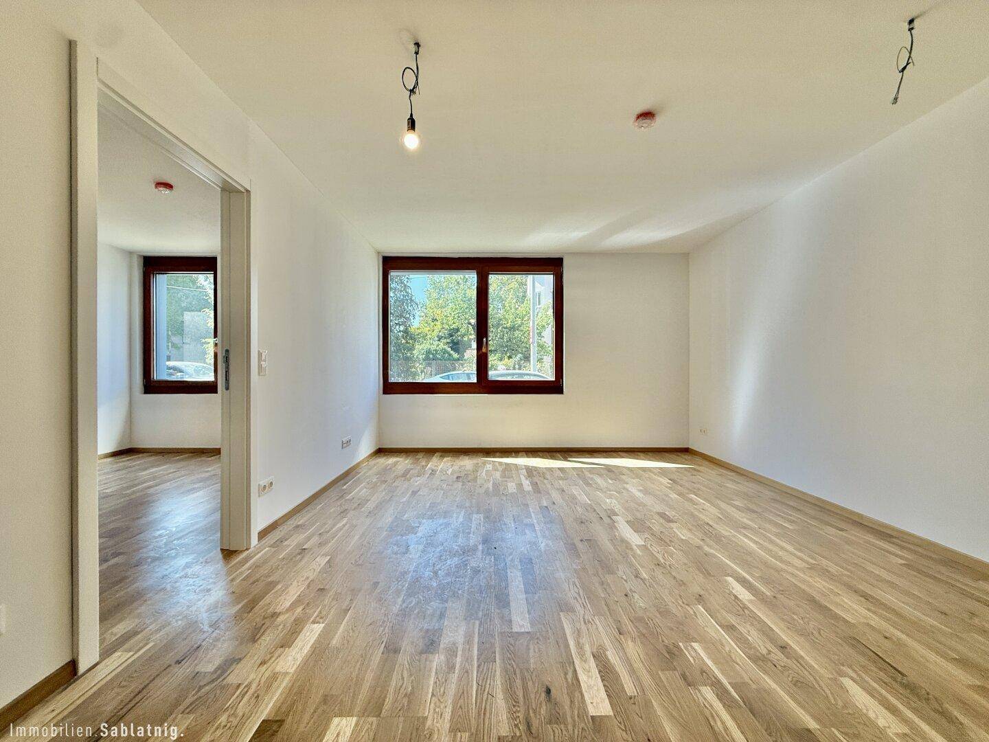Geräumiges, leeres Wohnzimmer mit Holzboden und großen Fenstern, bereit zur individuellen Gestaltung.