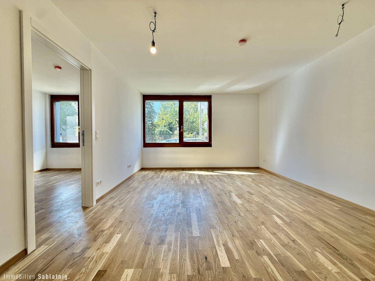 Helles, leeres Zimmer mit Holzboden und zwei Fenstern, ideal als Wohn- oder Schlafzimmer.