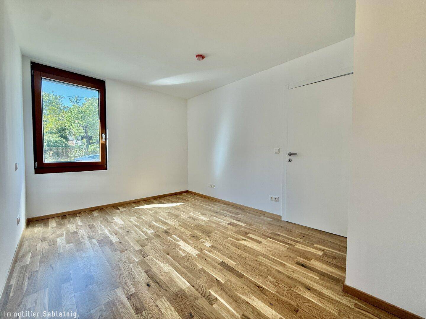 Leeres Schlafzimmer mit Holzboden und einem Fenster, bereit zur individuellen Einrichtung.