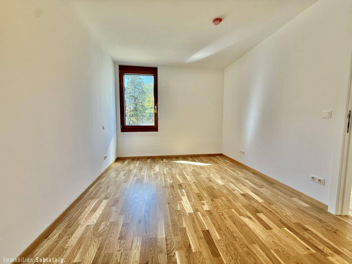 Helles, leeres Schlafzimmer mit Holzboden und Fenster, ideal für ein Kinder- oder Gästezimmer.