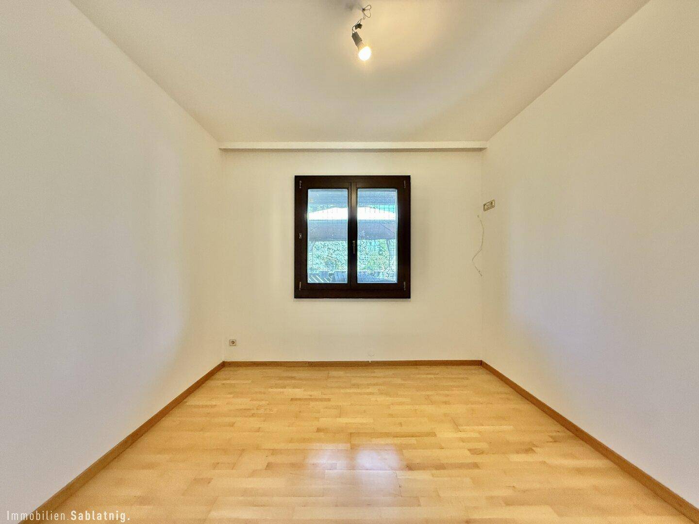 Leeres Schlafzimmer mit Parkettboden und Fenster, bereit für persönliche Einrichtung.