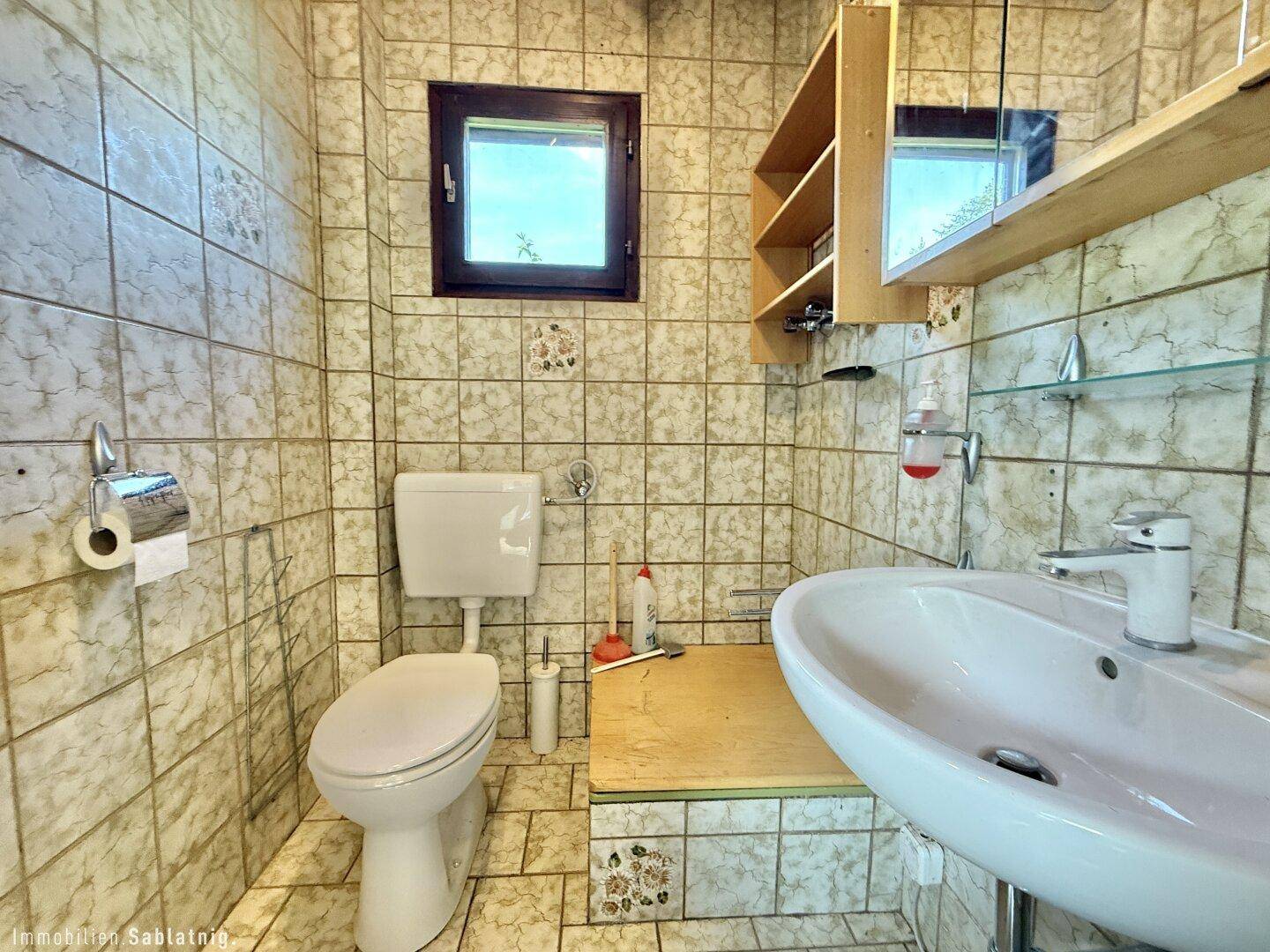 Badezimmer mit gemusterten Fliesen, WC, Waschbecken und Fenster für Tageslicht.