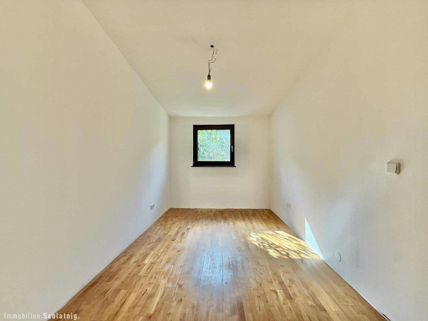 Helles Zimmer mit Holzfußboden und Fenster, vielseitig nutzbar als Schlaf- oder Arbeitszimmer.