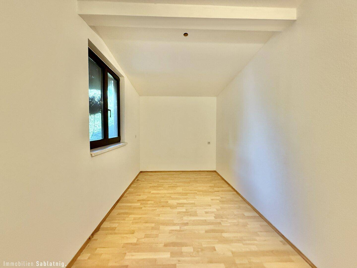 Leeres Zimmer mit Holzfußboden und Fenster, ideal für individuelle Gestaltung.