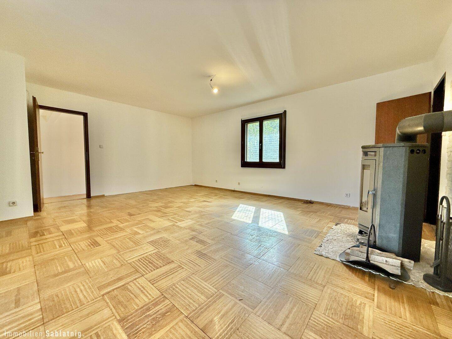 Geräumiges Wohnzimmer mit Parkettboden und Kaminofen, bereit zur individuellen Gestaltung.
