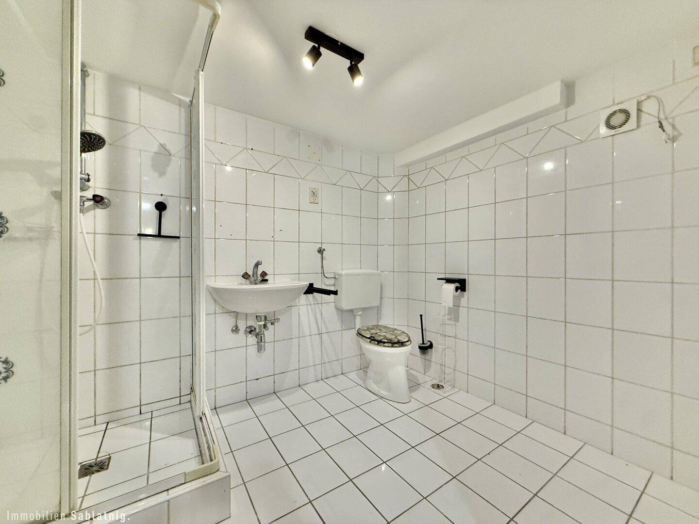 Badezimmer im Untergeschoss mit weißen Fliesen, Dusche, WC und Waschbecken.