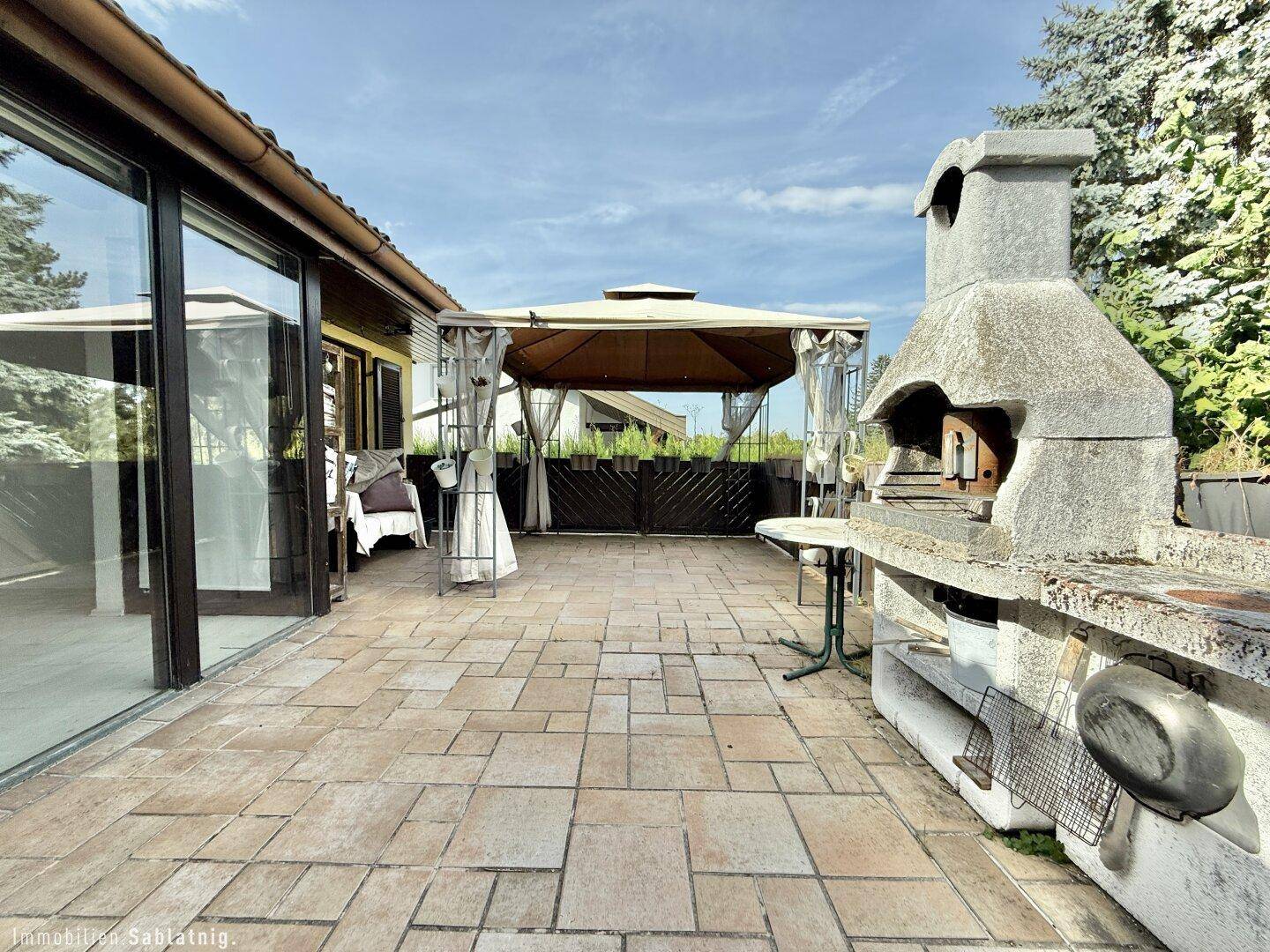Große gepflasterte Terrasse mit gemauertem Grill und schattenspendendem Pavillon.