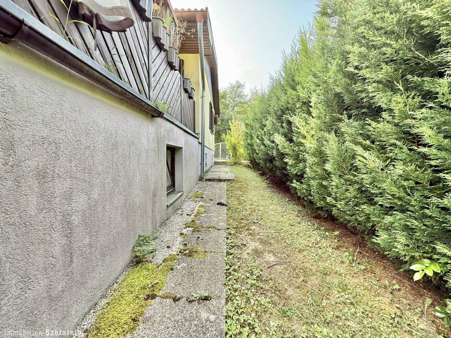 Seitenansicht des Hauses mit einem schmalen Weg und einer hohen Hecke.