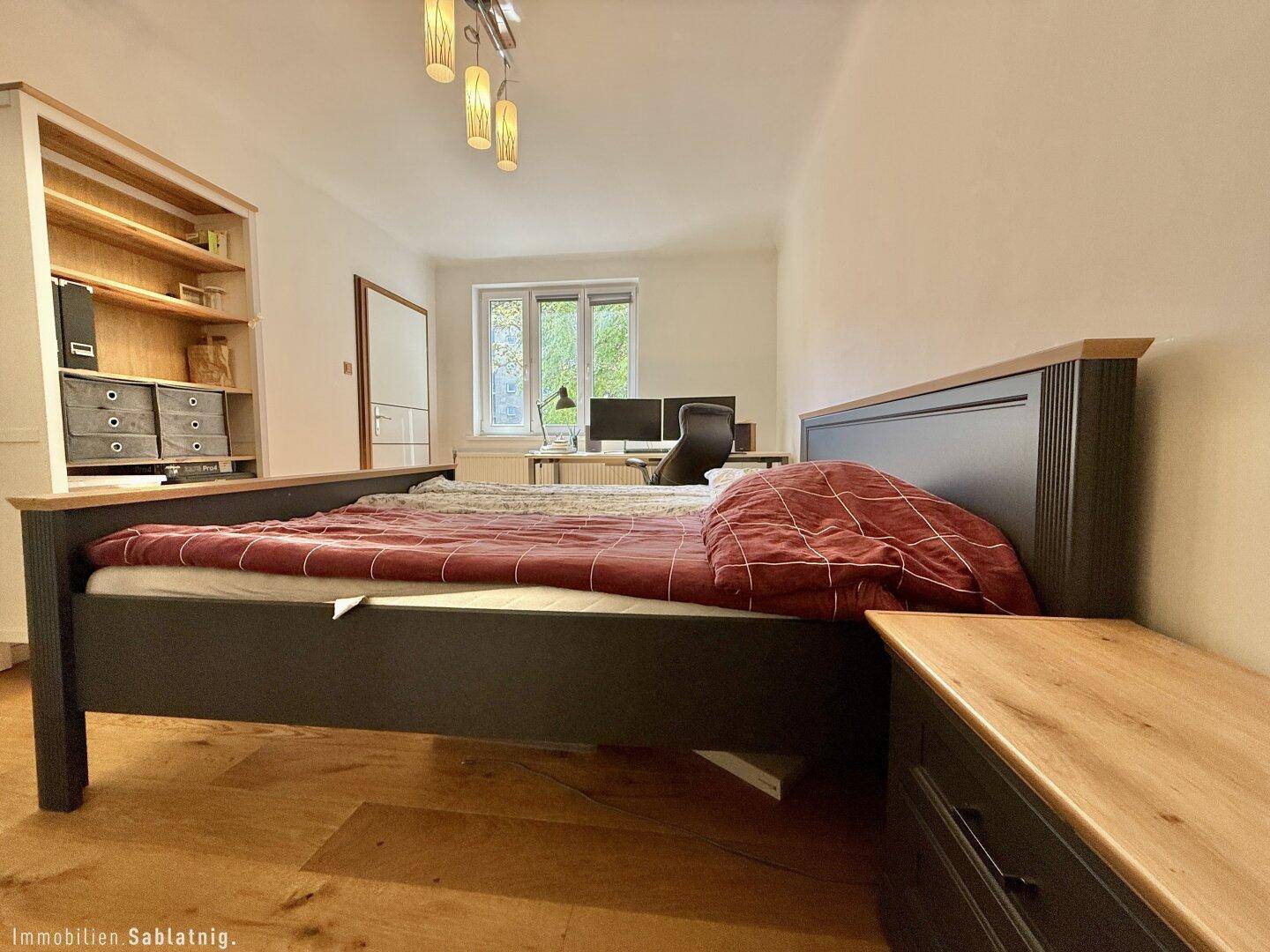 Helles Schlafzimmer mit Holzbett, Nachttisch und Blick ins Grüne.