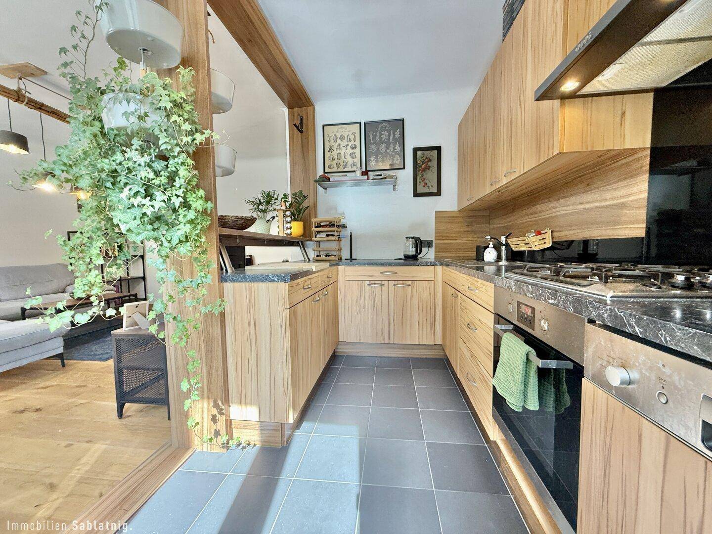 Funktionale Küche mit Holzfronten, dunkler Arbeitsplatte und Fliesenboden.