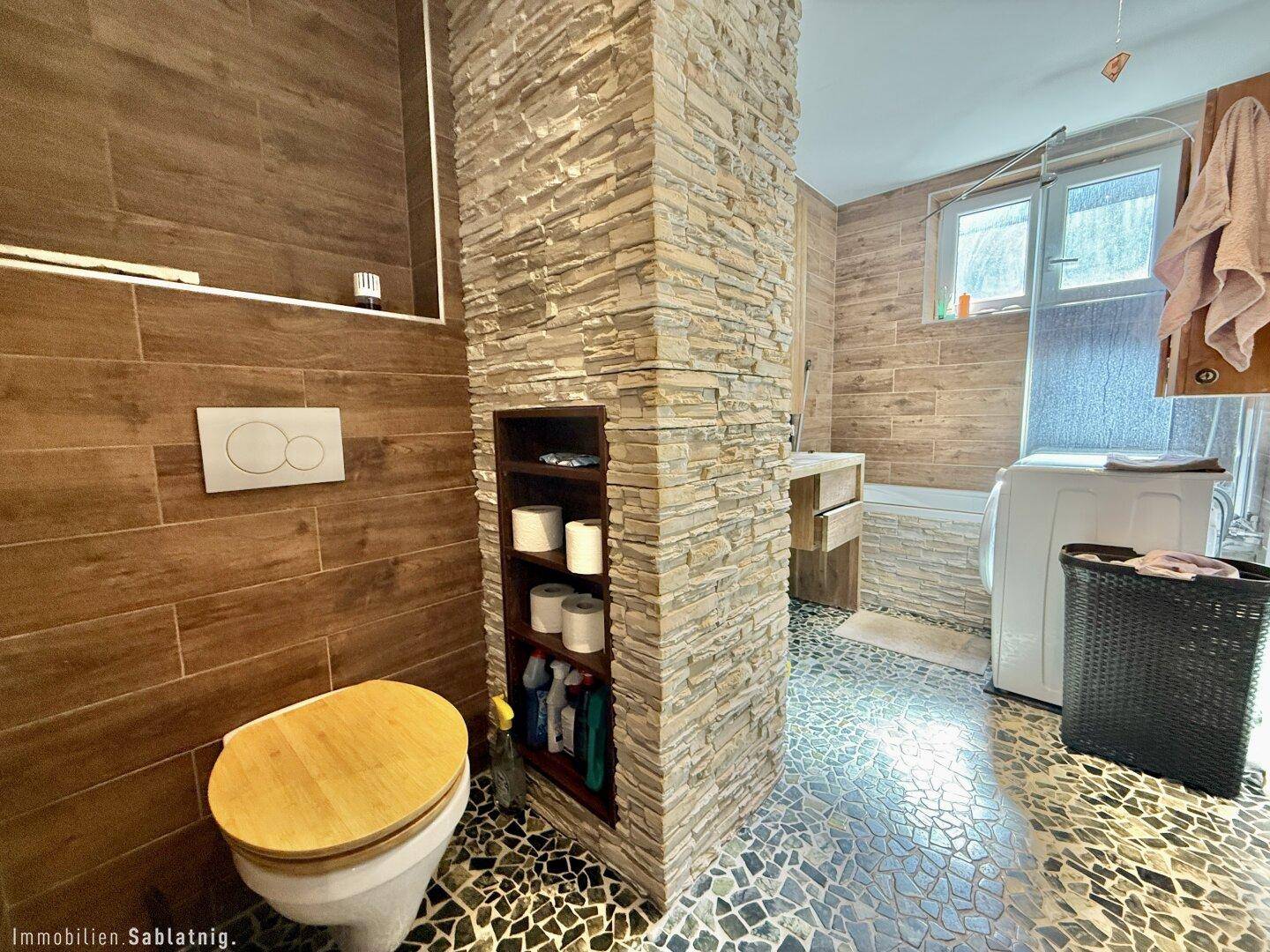 Badezimmer mit WC, Waschmaschine und dekorativer Steinwandverkleidung.