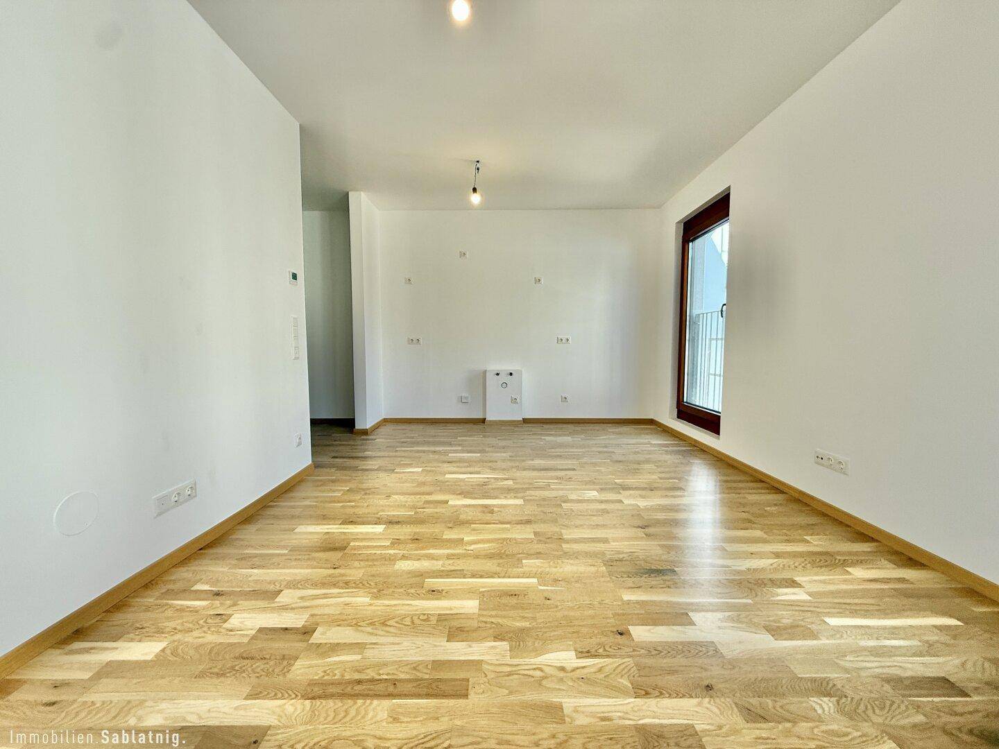 Geräumiges, leeres Wohnzimmer mit hellem Parkettboden und großen Fenstern, bereit zur Einrichtung.