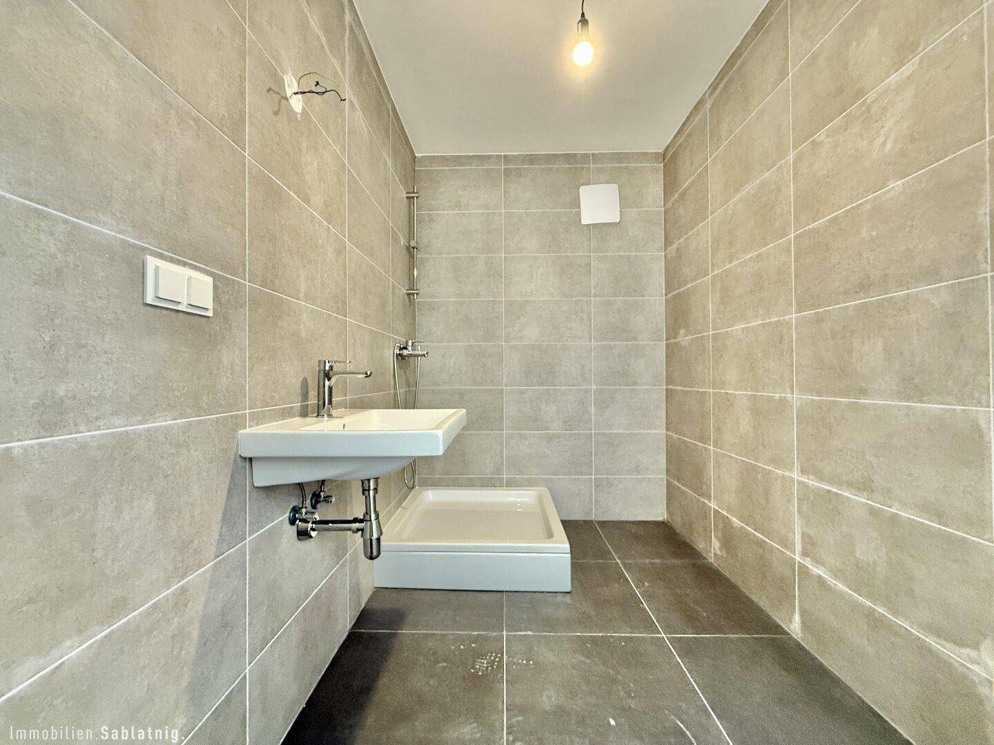 Modernes Badezimmer mit grauen Fliesen, Einzelwaschbecken und Duschbereich, funktional gestaltet.