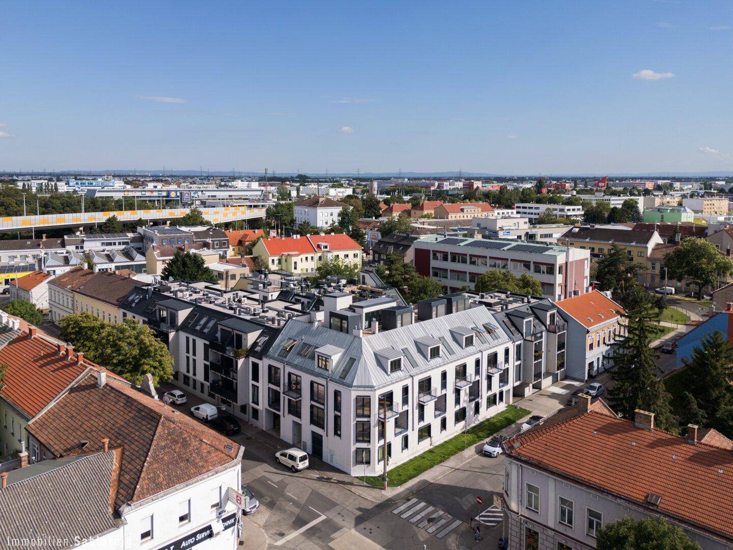 Luftaufnahme eines modernen Wohnkomplexes in einer städtischen Umgebung mit viel Grün und Infrastruktur.