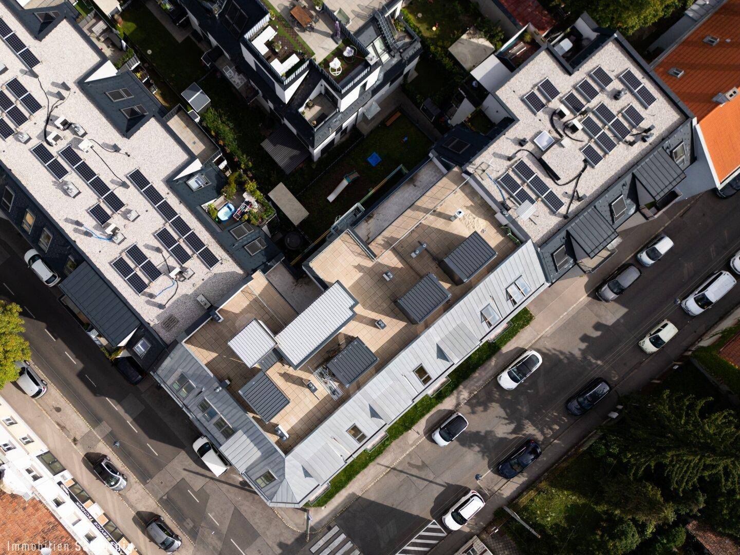 Vogelperspektive eines Wohnkomplexes mit Flachdächern, Solaranlagen und umliegenden Straßen, gut integriert.