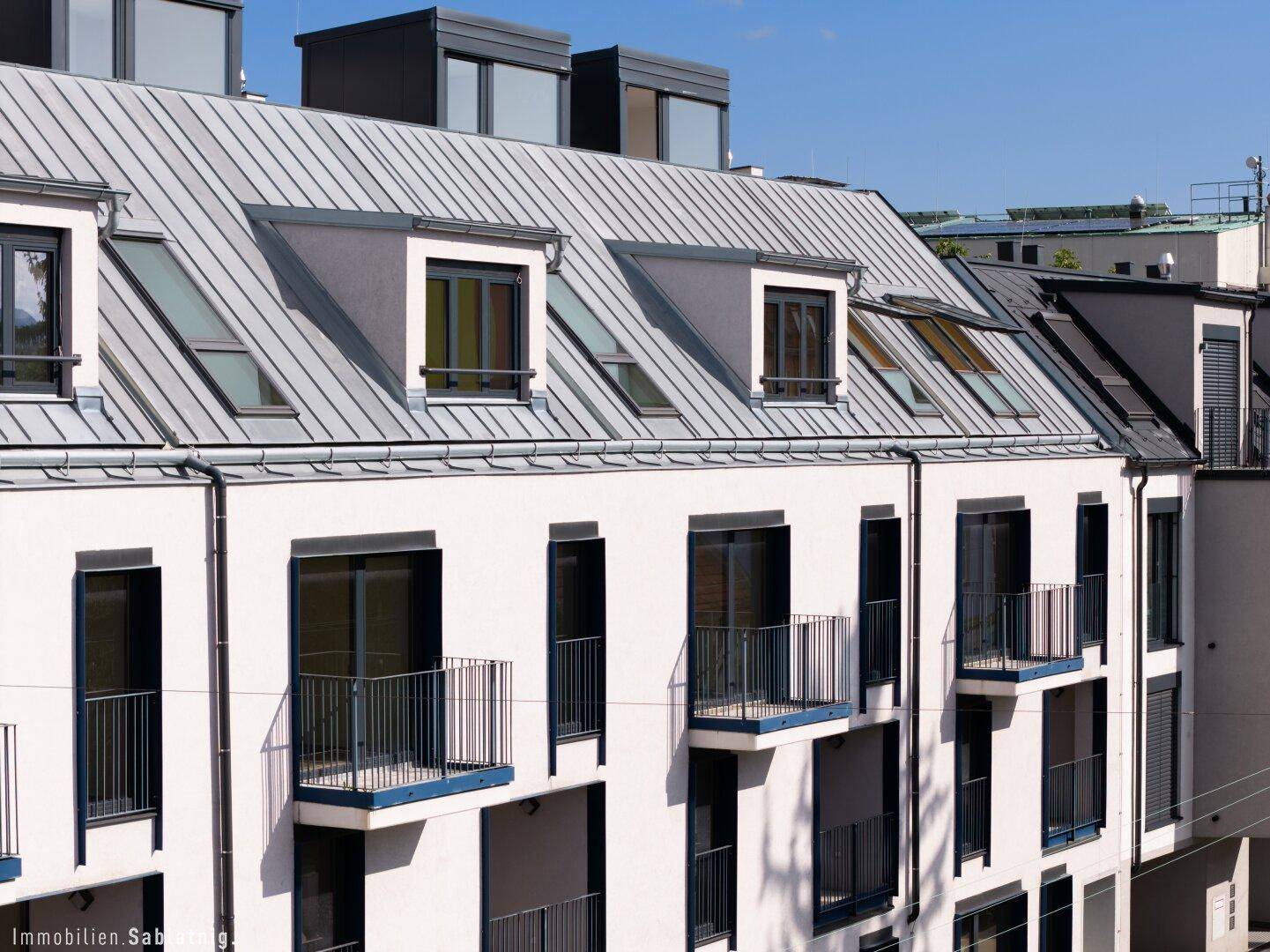 Dachlandschaft eines modernen Gebäudes mit Mansarddach, Dachfenstern und Balkonen, architektonisch interessant.